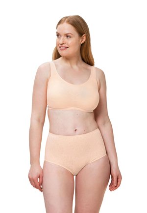 Kobieta o jasnej skórze i czerwonych włosach, ubrana w brzoskwiniowy, kwiatowy stanik bezszwowy oraz majtki z wysokim stanem, patrząca w bok i delikatnie się uśmiechająca.