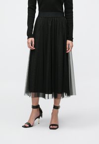 Melna tilla svārki ar caurspīdīgu slāni, dekorēti ar izkaisītiem rotājumiem un ribota jostasvietas joslu. Kombinēti ar melniem papēžu sandalēm ar potītes siksniņu.