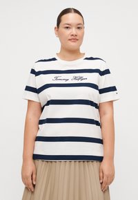 Hvid bomulds T-shirt med marineblå vandrette striber og broderet "Tommy Hilfiger" logo på forsiden. Korte ærmer og rund halsudskæring.