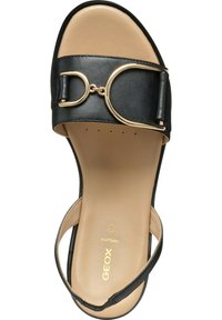 Sandale en cuir noir avec une large sangle et un matériel circulaire doré. Semelle intérieure beige clair avec la marque Geox. Design à bout ouvert et talon modéré.