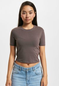 Brown cropped t-shirt with short sleeves, made of soft fabric. Paired with high-waisted light blue denim jeans. Simple round neckline.