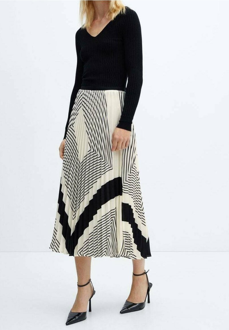 Top nero a coste con maniche lunghe abbinato a una gonna plissettata color crema con strisce geometriche nere. Tacchi neri a punta completano il look.