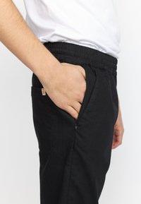 Zwarte sweatpants met een elastische tailleband, zijzakken en een klein rood label; gladde textuur en een casual ontwerp.