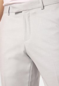Světle šedé kalhoty mají hladkou texturu, přiléhavý střih, boční kapsy a rovný střih s jemnými prošitými detaily.