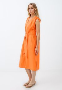 Oranje katoenen jurk met een V-hals, korte mouwen, tailleband en zijsplitten, met een gladde textuur en een knielange pasvorm.