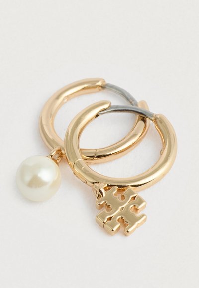 Χρυσά και ασημένια σκουλαρίκια κρίκοι με ένα μεγάλο λευκό μαργαρίτι και ένα διακοσμητικό γοτθικό σταυρό, διαθέτοντας λεία, γυαλισμένη επιφάνεια.