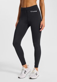 Sorte atletiske leggings lavet af strækbart stof, med en tætsiddende pasform og en lille hvid logo på taljebåndet. Stylet med hvide sneakers.