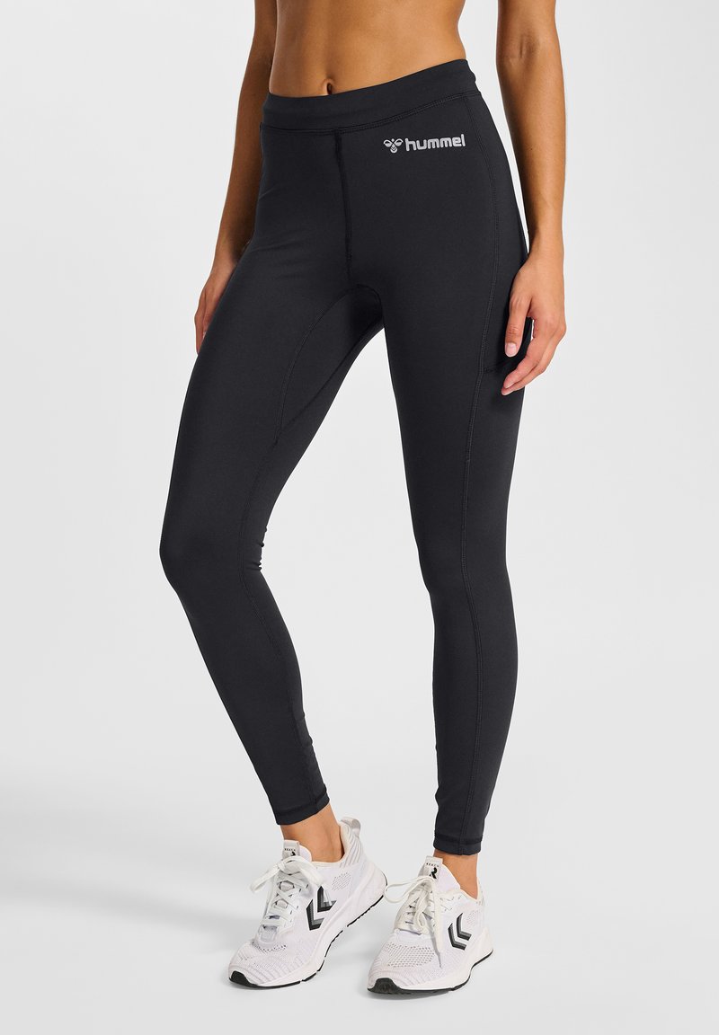 Sorte atletiske leggings lavet af strækbart stof, med en tætsiddende pasform og en lille hvid logo på taljebåndet. Stylet med hvide sneakers.