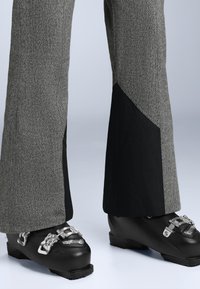 Szürke halszálkás sínadrág fekete szövet részekkel az alján, fekete sícsizmákkal, amelyek fém csatokkal rendelkeznek.