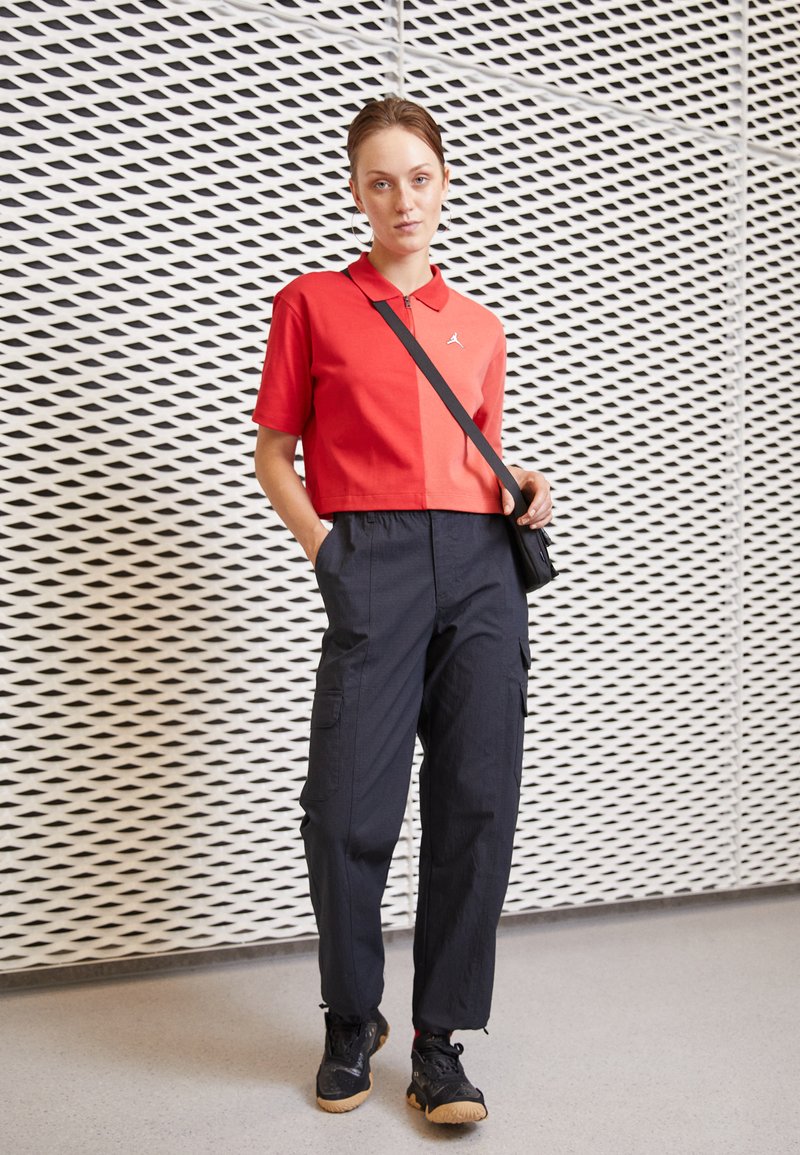 Rode cropped polo shirt met een kraag en logo, gecombineerd met marineblauwe cargo pants met zakken, en zwarte sportschoenen met een gumsole.