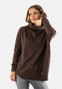 Maglione a collo alto marrone con colletto e orlo a costine, dotato di maniche lunghe e vestibilità comoda. Piccolo logo dettagliato in basso a sinistra.