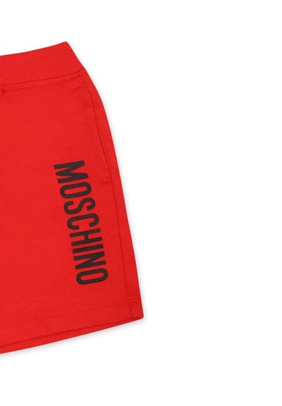 Shorts rossi in cotone con il logo nero "MOSCHINO" stampato verticalmente sul lato sinistro. Vita elastica e superficie liscia.