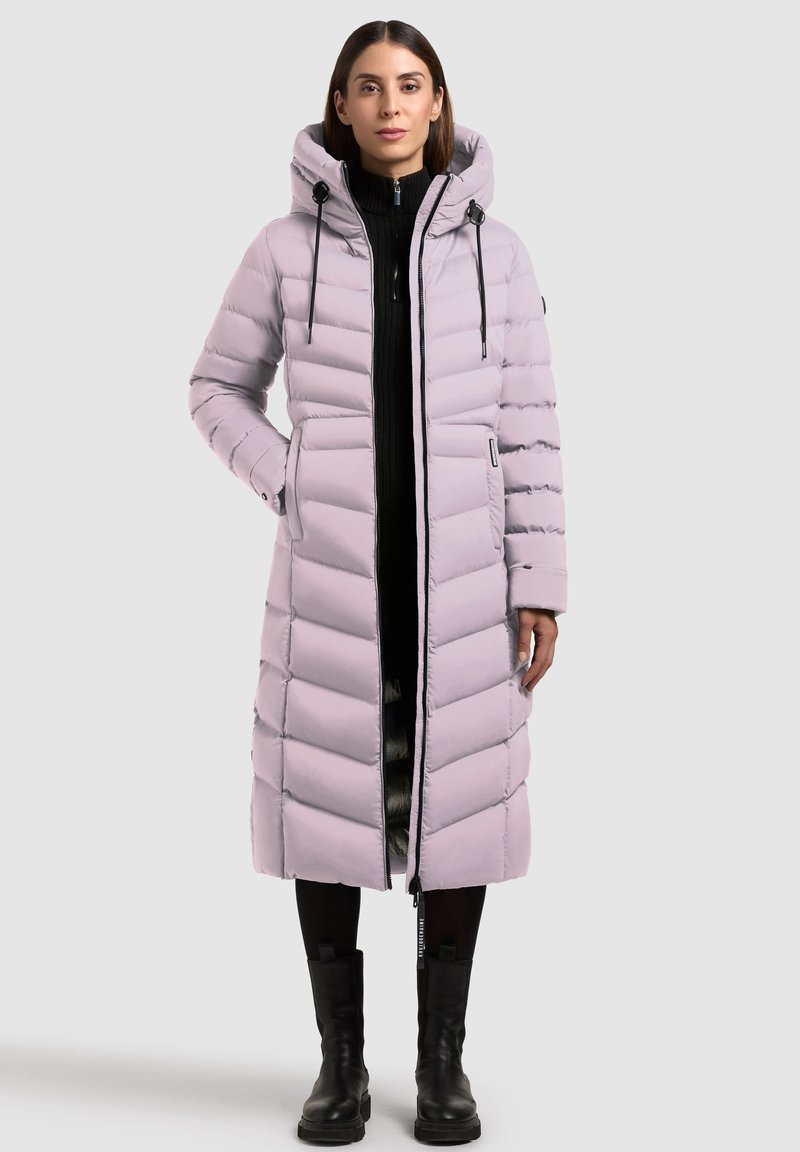 Svetlofialová páperová bunda s chevronovým prešívaním, veľkou kapucňou, zipsom a nastaviteľnými šnúrkami. Nosená cez čierny sveter a nohavice.