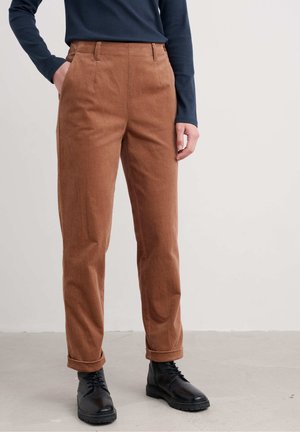 Braune Baumwollhose mit glatter Textur, taillierte Passform, zwei Seitentaschen und umgeschlagenen Bündchen, kombiniert mit schwarzen Schnürstiefeln.