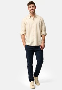 Lys beige linned skjorte, optrukne ærmer, knaplukning foran; mørkeblå bukser; lys beige sneakers. Enkle, afslappede look med løs pasform.