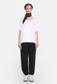 Biała, oversize'owa koszulka z krótkim rękawem, w połączeniu z czarnymi spodniami dresowymi ze sznurkiem i czarnym szalem z czerwonymi kwiatowymi akcentami. Całość uzupełniają białe sneakersy.