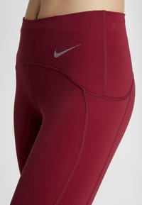 Leggings bordeaux in tessuto elasticizzato, vita alta, logo Nike argento, cuciture piatte e texture liscia per un comfort ottimale durante l'attività fisica.