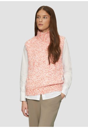 Gebreide roze en witte mouwloze coltrui met een gestructureerd patroon, gedragen over een wit shirt en gecombineerd met beige broeken.