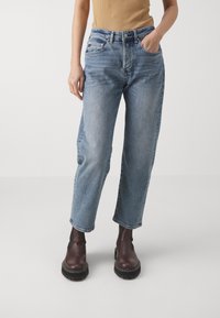 Jasnoniebieskie, wysokie dżinsy o luźnym kroju, wykonane z denimu z widocznymi szwami i pięcioma kieszeniami. Połączone z brązowymi botkami za kostkę.