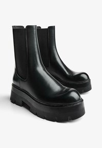 Cizme Chelsea din piele neagră, cu panouri elastice laterale, talpă groasă din cauciuc, vârf rotund și textură netedă.