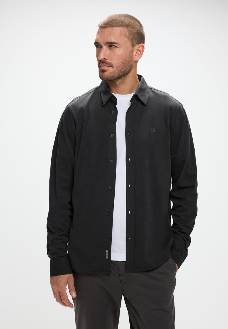 Svart skjorta med knappar i mjukt tyg, med klassisk krage, långa ärmar och en subtil logotyp på vänster bröst.