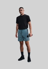 Mandens sorte kortærmede skjorte, tealfarvede shorts med elastisk linning og snøre, sort vandflaske og sorte sneakers. Glat stof, sporty design.