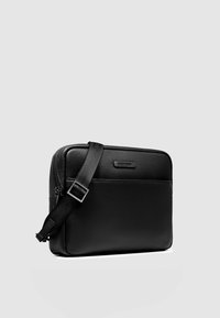 Schwarze Leder-Umhängetasche mit strukturierter Oberfläche, rechteckiger Form, verstellbarem Riemen und dezentem Branding auf der Vorderseite.