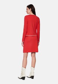 Red knit dress with long sleeves, white accent at the waist. A-line skirt with a smooth texture, paired with white heeled boots.