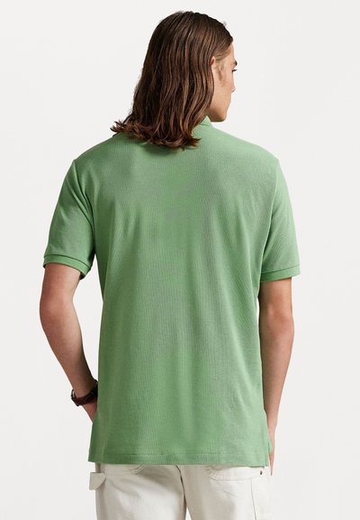 Zaļā polo krekls ar teksturētu audumu, īsām piedurknēm un klasisku apkakli, redzams no mugurpuses. Vienkāršs un pieguļošs dizains.