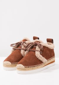 Brown suede ankle boots with beige faux fur lining, round toe, decorative laces, and woven jute platform sole.