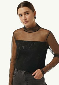 Schwarz Oberteil mit durchsichtigen, gepunkteten Ärmeln und hohem Kragen. Der Körper besteht aus einem strukturierten Stoff und hat eine enganliegende Silhouette, die ein modernes Design betont.