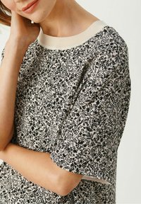 Bloemrijke t-shirt in crème en zwart, met korte mouwen en een ronde halslijn, gemaakt van zachte katoen met een fijn patroon van bladeren en bloemen.