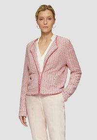 Roze tweed jasje met een gestructureerd patroon, cropped ontwerp, nietched kraag en bloemvormige hardwareaccenten. Draagt over een witte blouse.