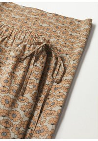 Tissu à motif floral marron avec une ceinture froncée et des liens à nouer. Le fond est de couleur beige clair.