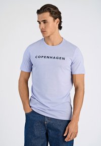 Vaaleanlila lyhythihainen t-paita, jossa rinnassa on mustana painettuna "COPENHAGEN" ja "LINDBERGH". Pehmeää kangasta, jossa pyöreä pääntie.