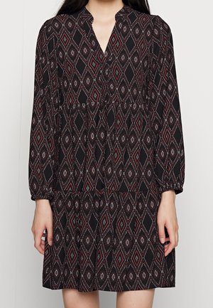 Vestido negro con un patrón de diamantes en rojo y blanco. Tiene mangas largas, cuello en V y un diseño de falda en capas.