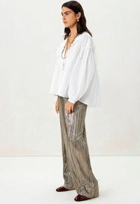 Witte blouse met gerimpelde accenten en ballonmouwen; metallic geplooide zilveren broek; donkerrode hakken; gelaagde kettingen.