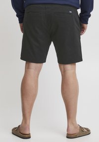 Pantalones cortos de algodón negro con una textura suave y corte recto. Cuenta con dos bolsillos traseros y una pequeña etiqueta en la cintura.