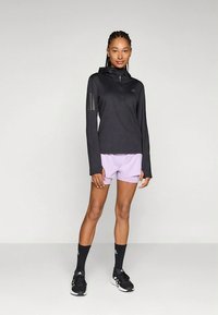 Top desportivo preto de manga comprida com fecho de correr até meio e detalhe de três riscas, combinado com calções lilás claros e meias pretas até ao tornozelo.