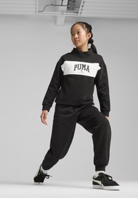 Chándal deportivo en blanco y negro con cuello de cremallera y logo, que presenta un corte holgado, puños acanalados y joggers negros ajustados a juego.