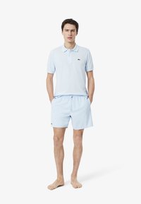 Lichtblauw polo shirt met korte mouwen en lichtblauwe shorts. Beide artikelen hebben een klein groen logo. De stof lijkt glad en casual.