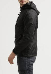 Zwarte hoodie met een gladde, lichtgewicht textuur. Beschikt over een voorzak en elastische manchetten. Gepromoot met donkere, versleten jeans.