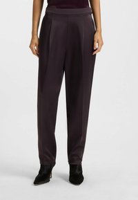 Donkerpaarse wijde broek van een gladde stof, met een hoge taille, plooien en een getailleerde pasvorm, gecombineerd met zwarte hoge hakken.