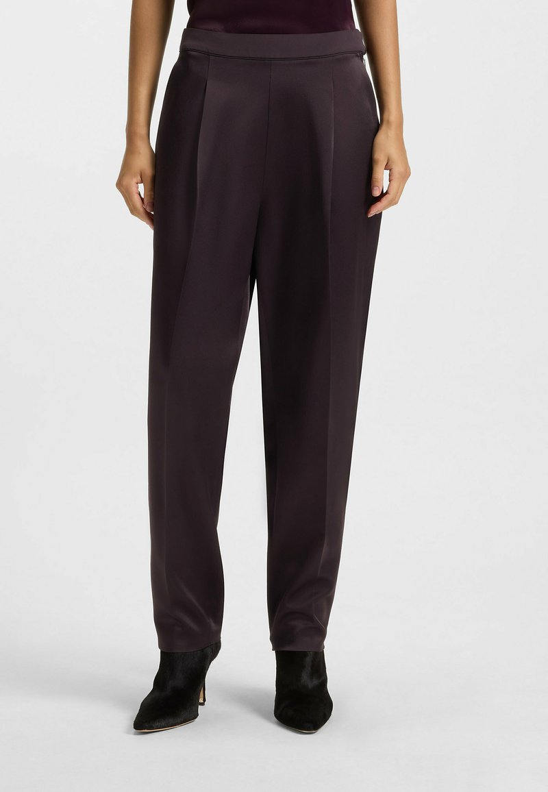 Donkerpaarse wijde broek van een gladde stof, met een hoge taille, plooien en een getailleerde pasvorm, gecombineerd met zwarte hoge hakken.