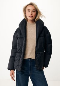 Doudoune noire avec un col haut et un design oversized. Présente une finition brillante et une fermeture éclair à l'avant, portée par-dessus un pull léger et un jean foncé.