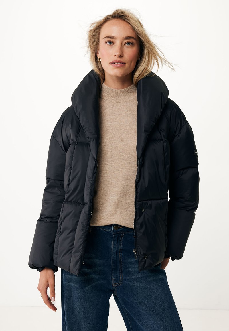 Doudoune noire avec un col haut et un design oversized. Présente une finition brillante et une fermeture éclair à l'avant, portée par-dessus un pull léger et un jean foncé.