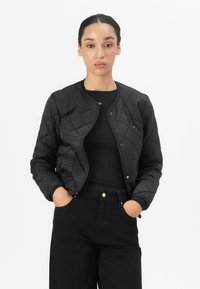 Black quilted bomber jacket with a round neckline, snap buttons, and ribbed cuffs. Paired with a fitted black top and high-waisted black pants.
