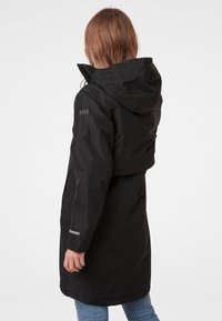 Zwarte waterdichte jas met capuchon, voorzien van een cropped ontwerp, ritszakken en reflecterende details op de mouwen.