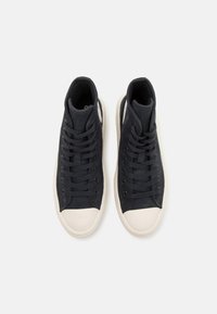 Zapatillas altas negras de lona, con punta de goma blanca y diseño de cordones. Textura suave con detalles mínimos.