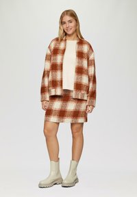 Bruine en crèmekleurige geruite jas met bijpassende rok, gemaakt van een gestructureerde stof. Gepaard met beige enkellaarsjes. Eenvoudig, modern ontwerp.